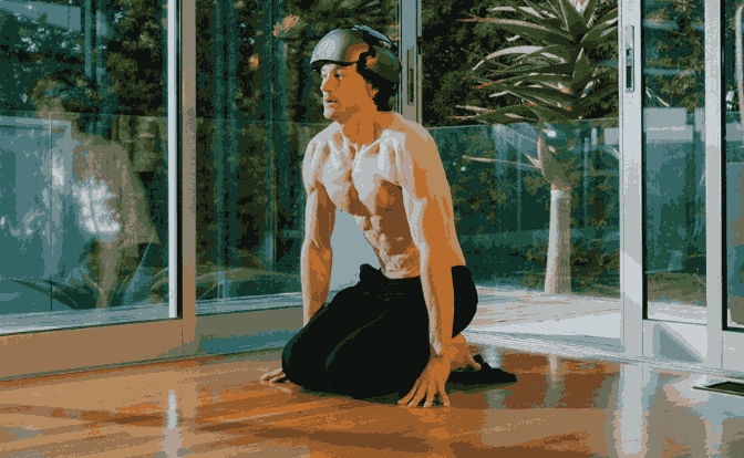 Man wearing a helmet kneels on the floor in front of glass doors, appearing to practice breathing exercises related to Byran Johnson Hyperbaric Chamber.